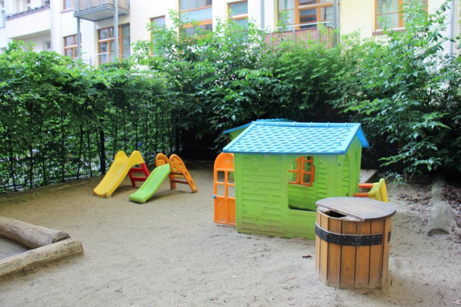 Der grüne Garten der Kita Kopernikushof mit Spielhaus und Gebäude im Hintergrund